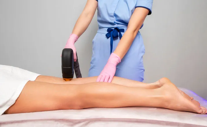 A practitioner performing a laser hair removal treatment on a patient's leg